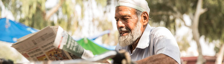 Older Indian man reading newspaper outdoors