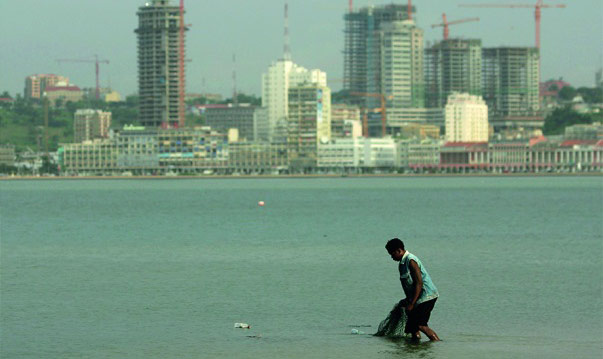Man gathering up fishing net in bay with a city backdrop