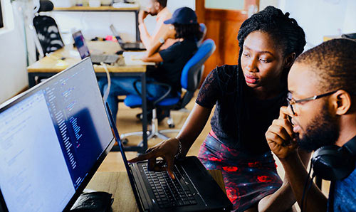 woman and man sitting in front of a computer monitor. 